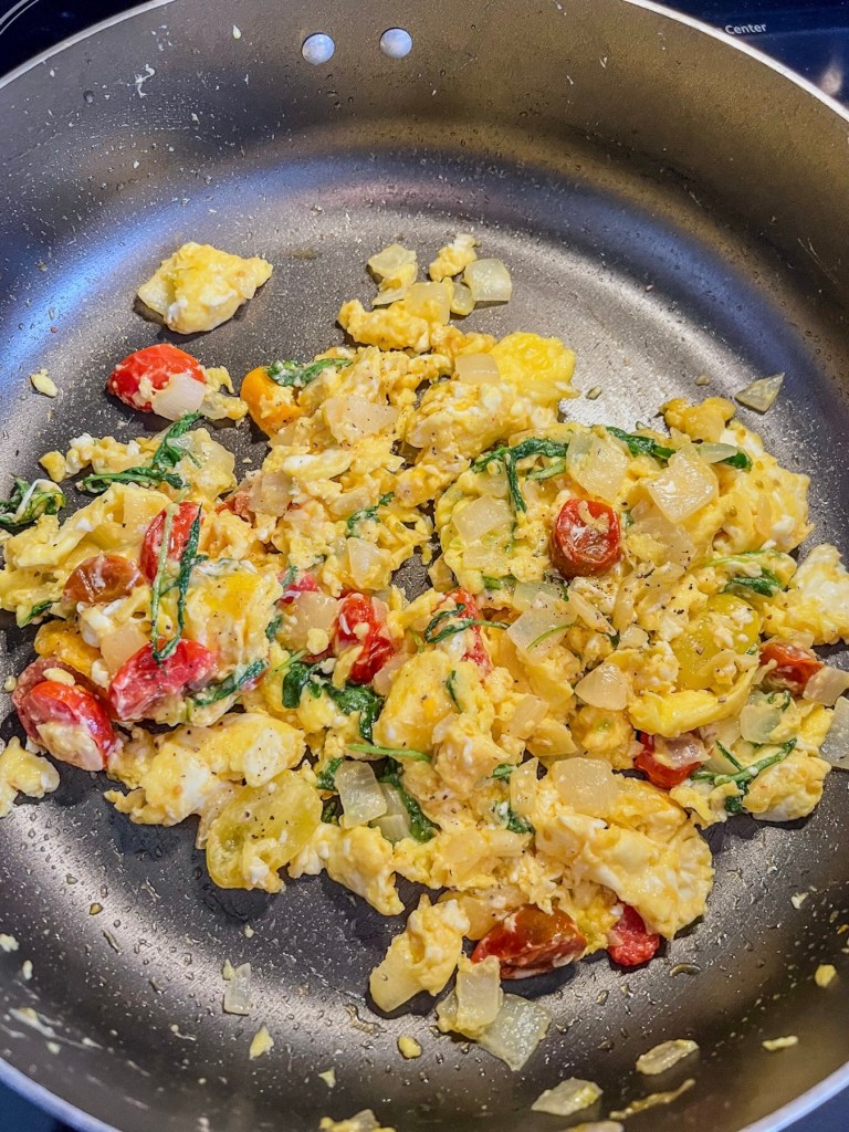 Scrambled eggs with fresh veggies, herbs and cheese in a skillet