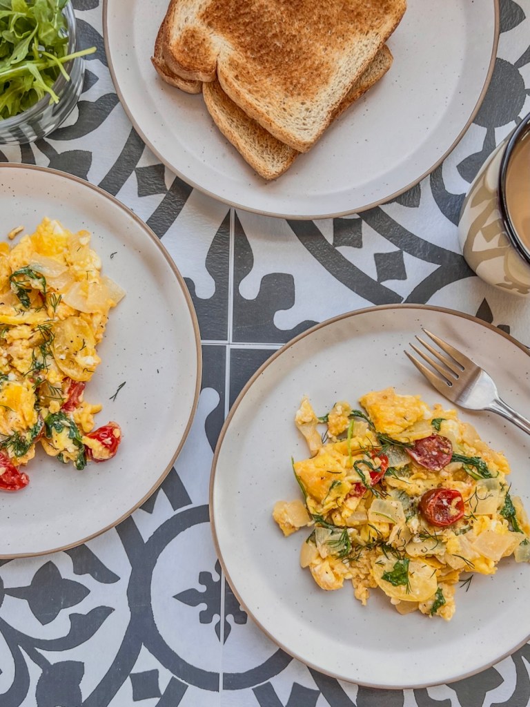 Scrambled eggs with arugula and tomatoes served with some buttered toast and coffee