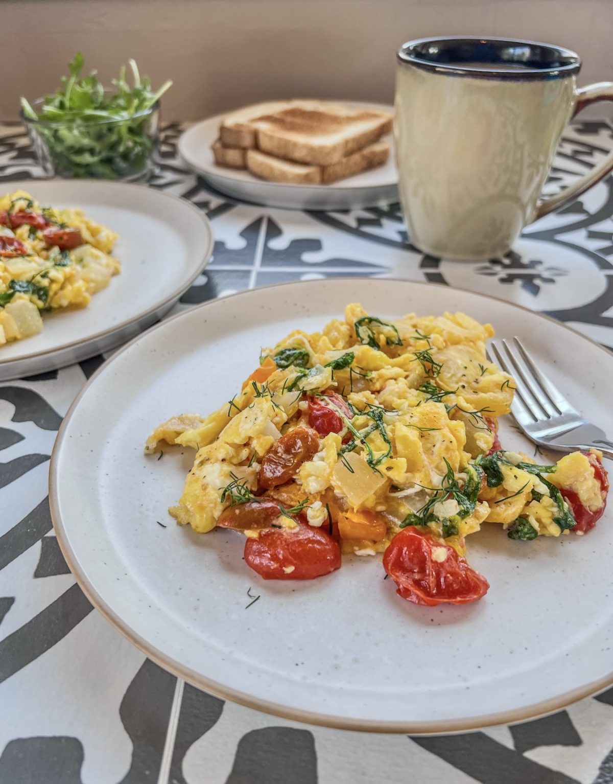 Scrambled eggs with arugula and tomatoes on a plate with some fresh dill and lemon juice on top
