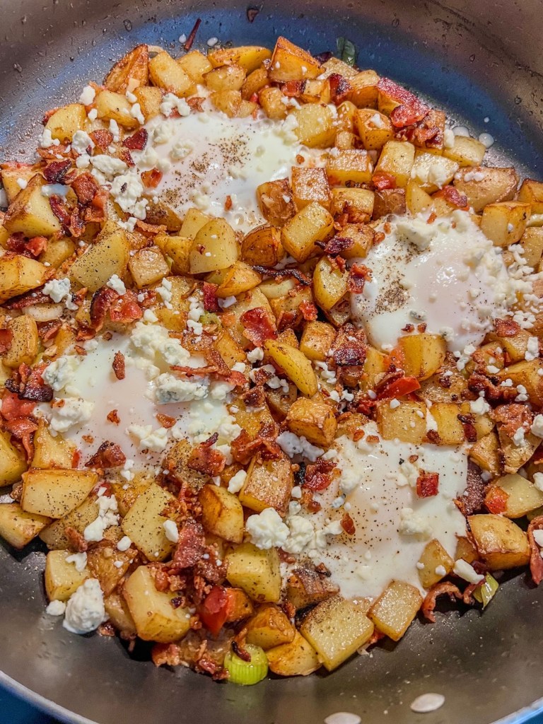 Bacon veggie breakfast hash in a skillet with some eggs nestled inside and bacon scattered over the top
