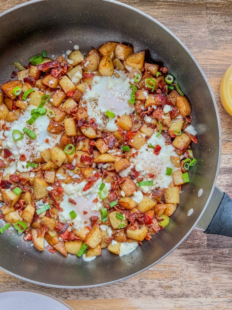 A one pot breakfast hash with bacon, green onion, and gorgonzola cheese garnished on top