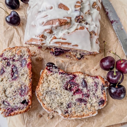 Cherry vanilla loaf cake that's been drizzled with vanilla glaze and sliced for serving