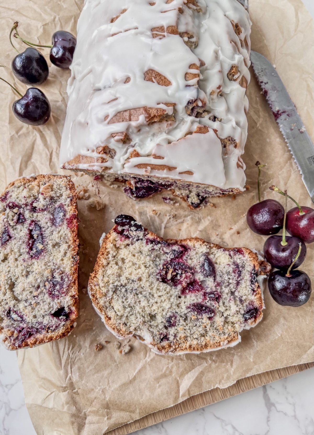 Cherry vanilla loaf cake with a homemade vanilla glaze over top and some fresh cherries on the side