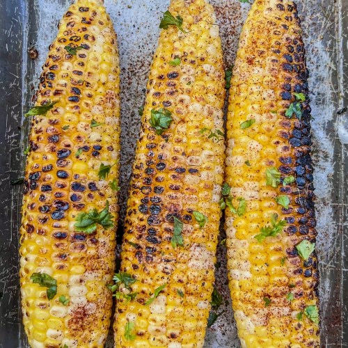 Easy char-grilled corn on the cob in a pan with some butter, salt, freshly cracked black pepper, chili powder, and cilantro on top.