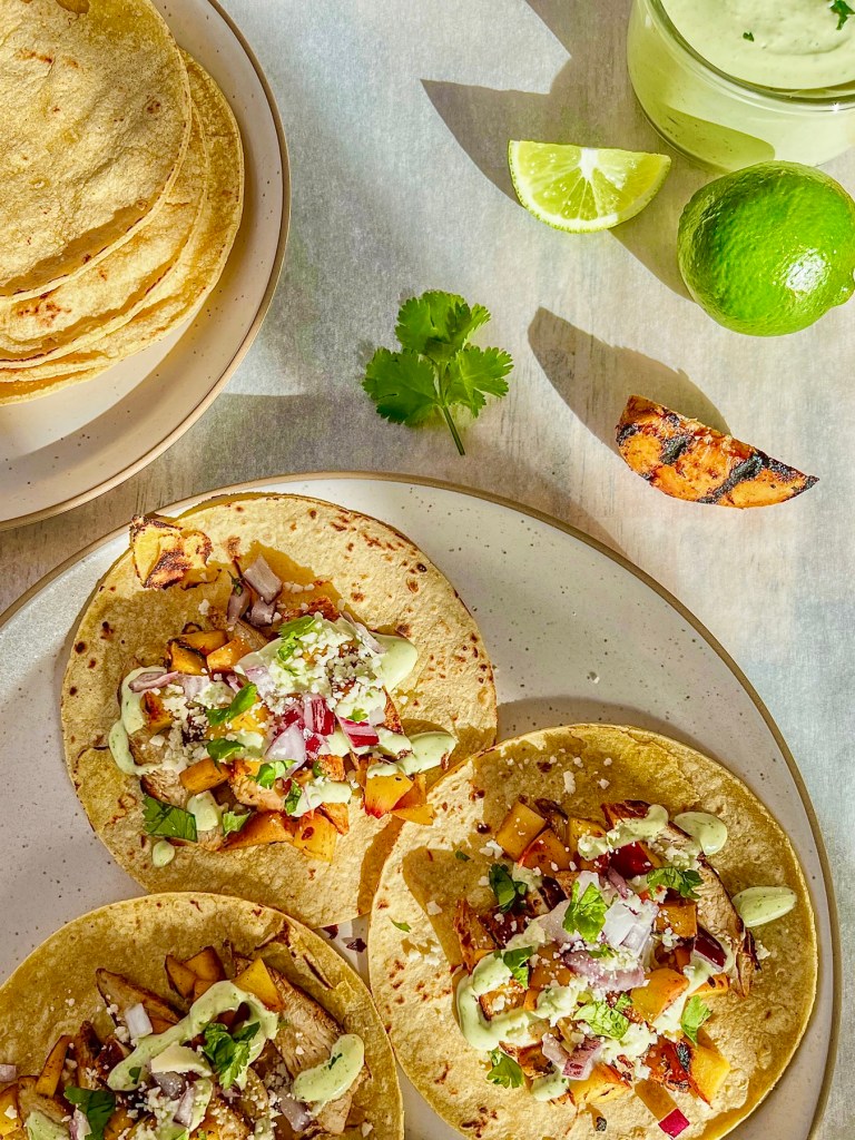 Grilled chicken street tacos with peaches and cilantro, cilantro lime crema, red onion, cotija cheese, and lime wedges on the side.