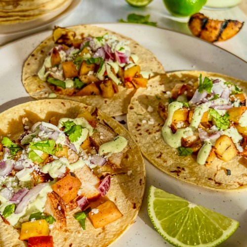 Grilled chicken street tacos with chili peaches, cilantro lime crema, cotija cheese, cilantro, red onion, and lime wedges on a plate