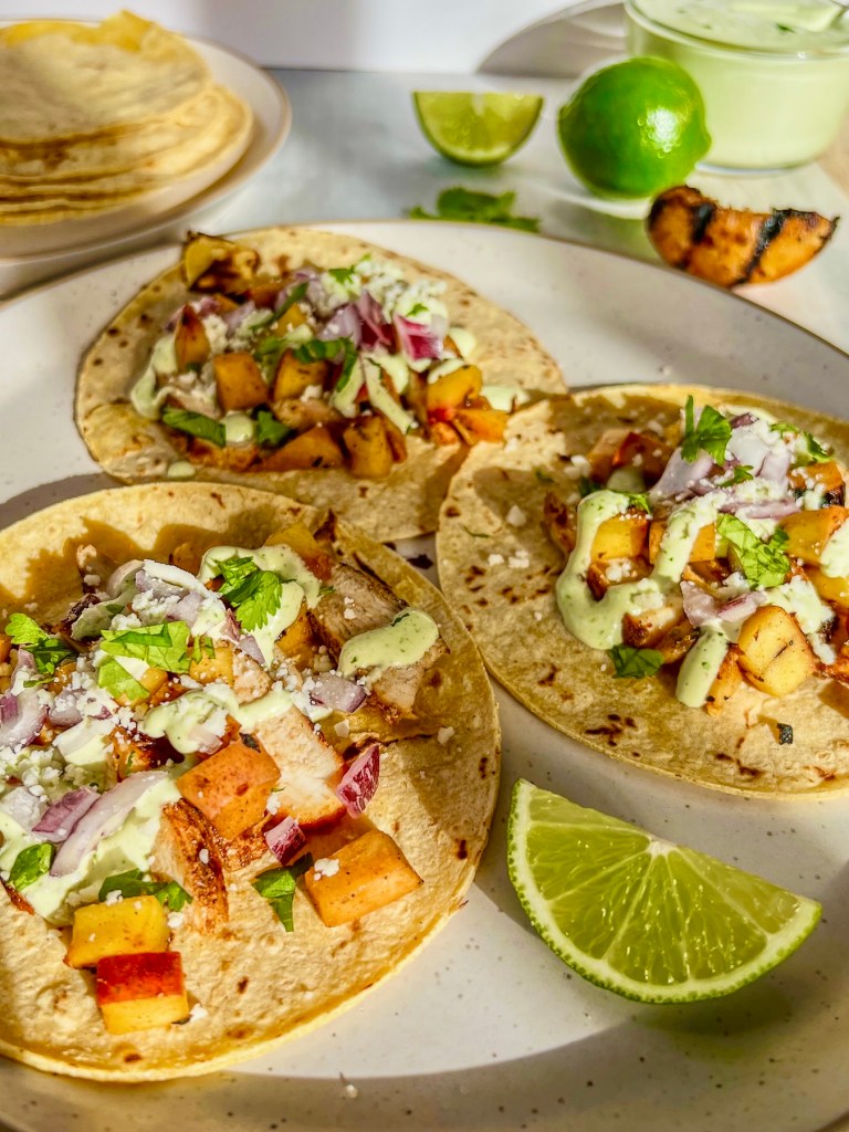Grilled chicken street tacos with chili peaches, cilantro lime crema, cotija cheese, cilantro, red onion, and lime wedges on a plate