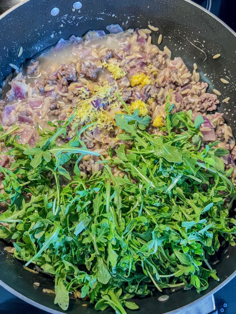 A creamy one pan meal cooking with some newly added arugula, lemon juice, and lemon zest