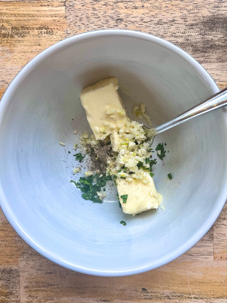 Butter, garlic, basil, and pepper in a mixing bowl to make an herb butter