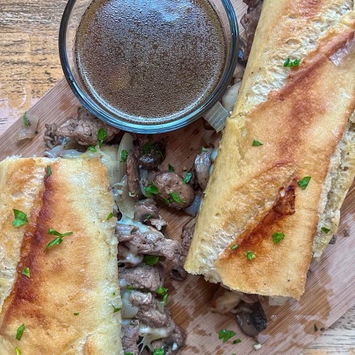 Steak melt with some fresh parsley scattered on top and some au jus for dunking.