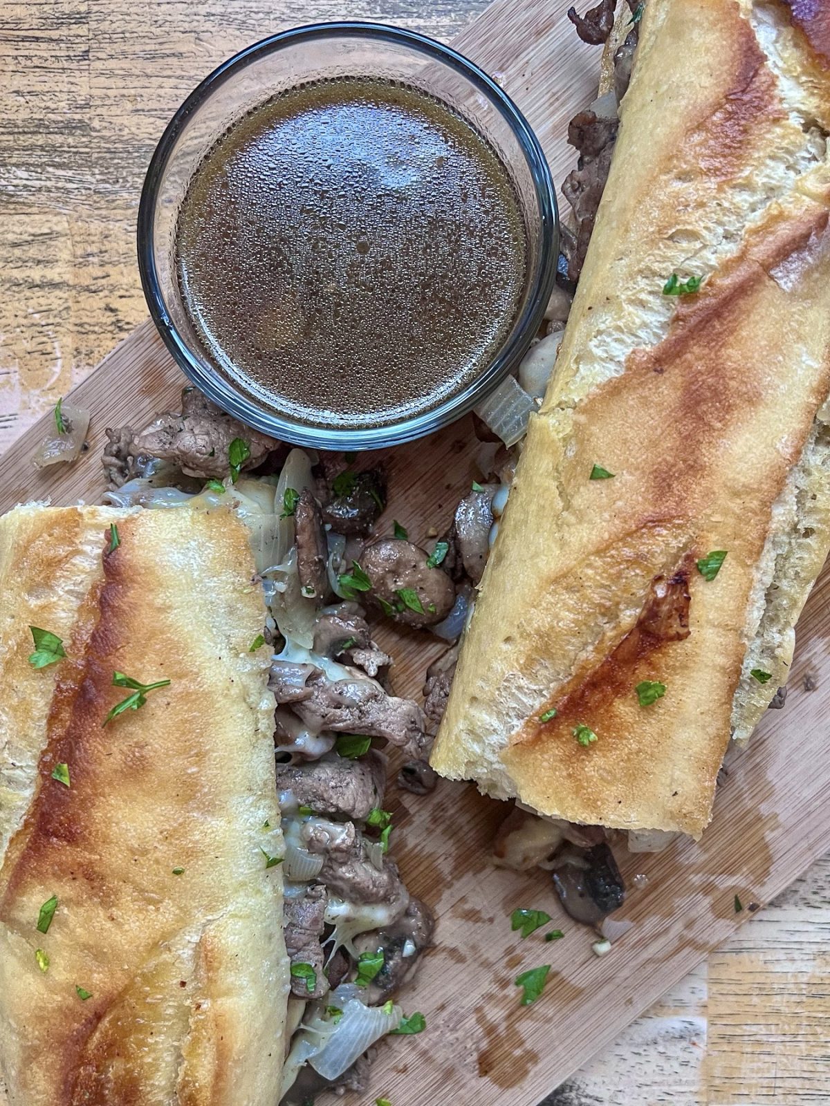 Steak melt with some fresh parsley scattered on top and some au jus for dunking.