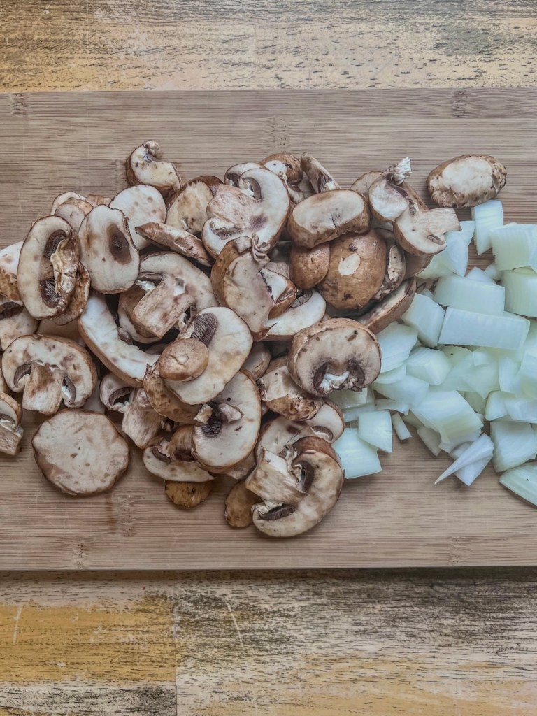 Mushrooms and Vidalia onion prepped on a cutting board