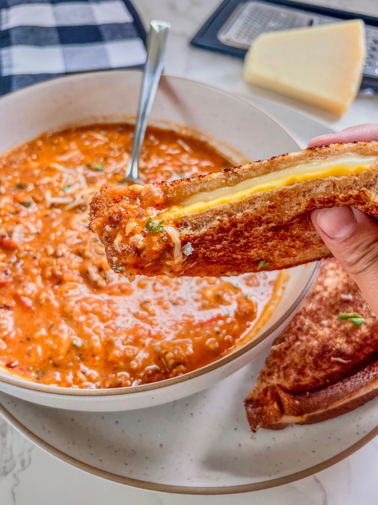 Tomato basil sausage soup in a bowl with a grilled cheese being dunked into it