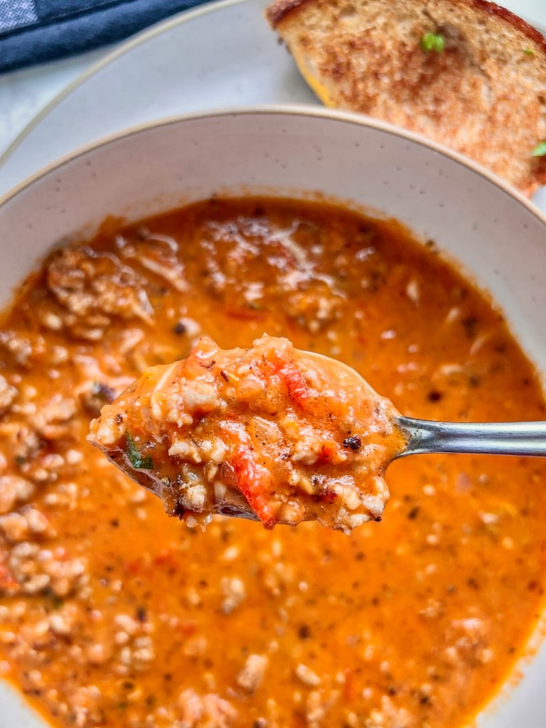 Tomato basil sausage soup in a bowl with a spoon scooping some out