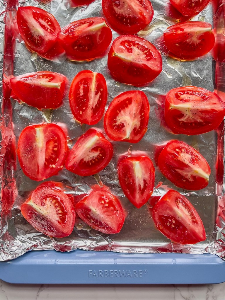 Tomatoes that have been quartered and drizzled with oil and spices on a baking sheet