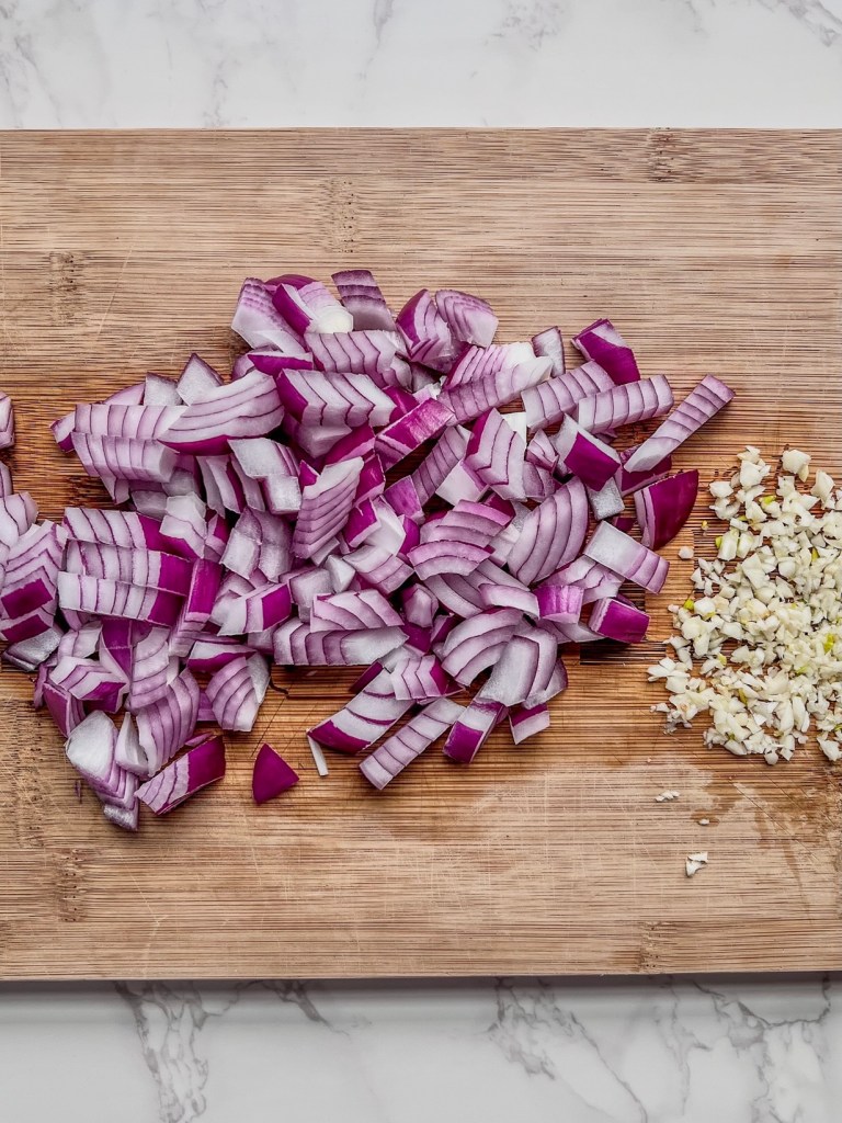 Red onion and garlic prepped on a cutting board