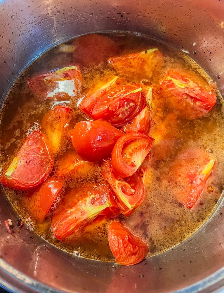 Blistered tomatoes, broth, onions, garlic, and spices simmering in a pot