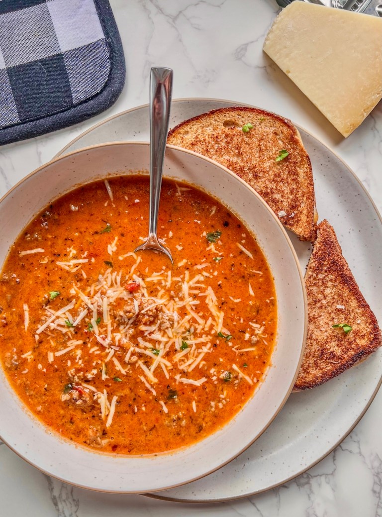 Tomato basil sausage soup in a bowl with some grilled cheese and a parmesan wedge off to the side.