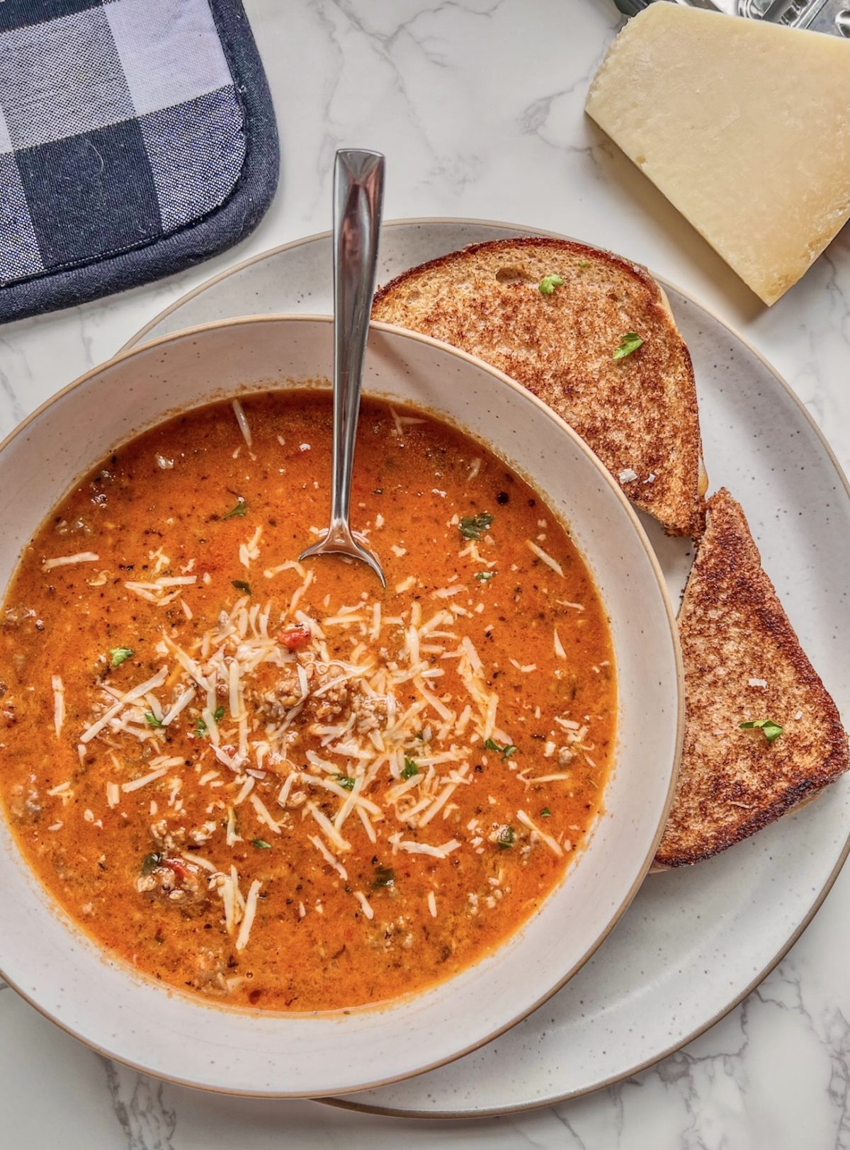 Tomato basil sausage soup in a bowl with some parmesan and a grilled cheese off to the side.