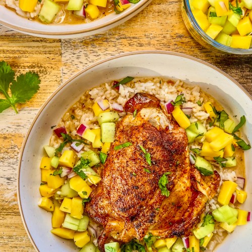 Tropical chicken thigh bowls with fresh cilantro on top and some cucumber mango salsa off to the side