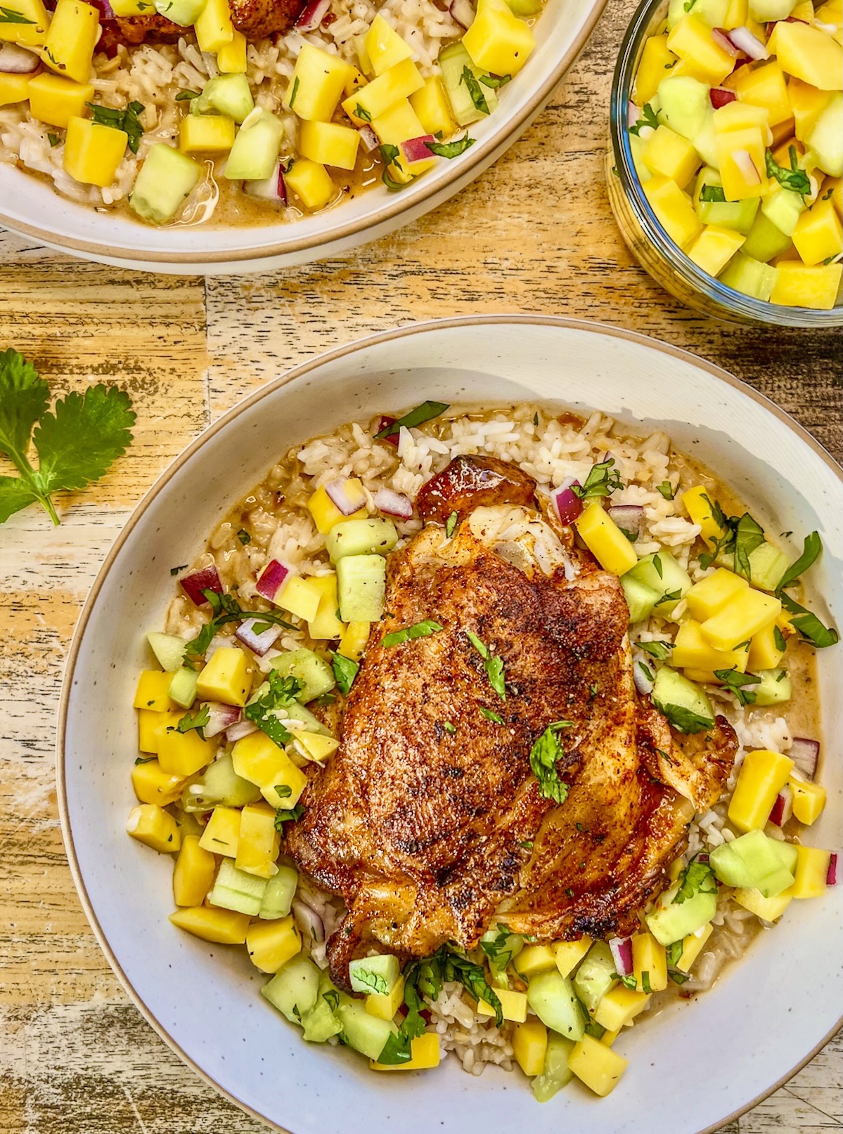 Tropical chicken thigh bowls with a fresh cucumber mango topping and cilantro for garnish.