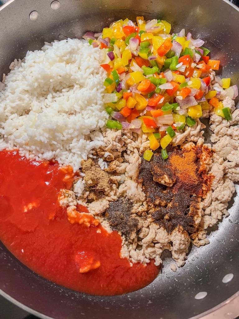 Ground chicken, cooked white rice, tomato sauce, bell peppers, onions, jalapeño, and a variety of spices cooking in a skillet on the stove.