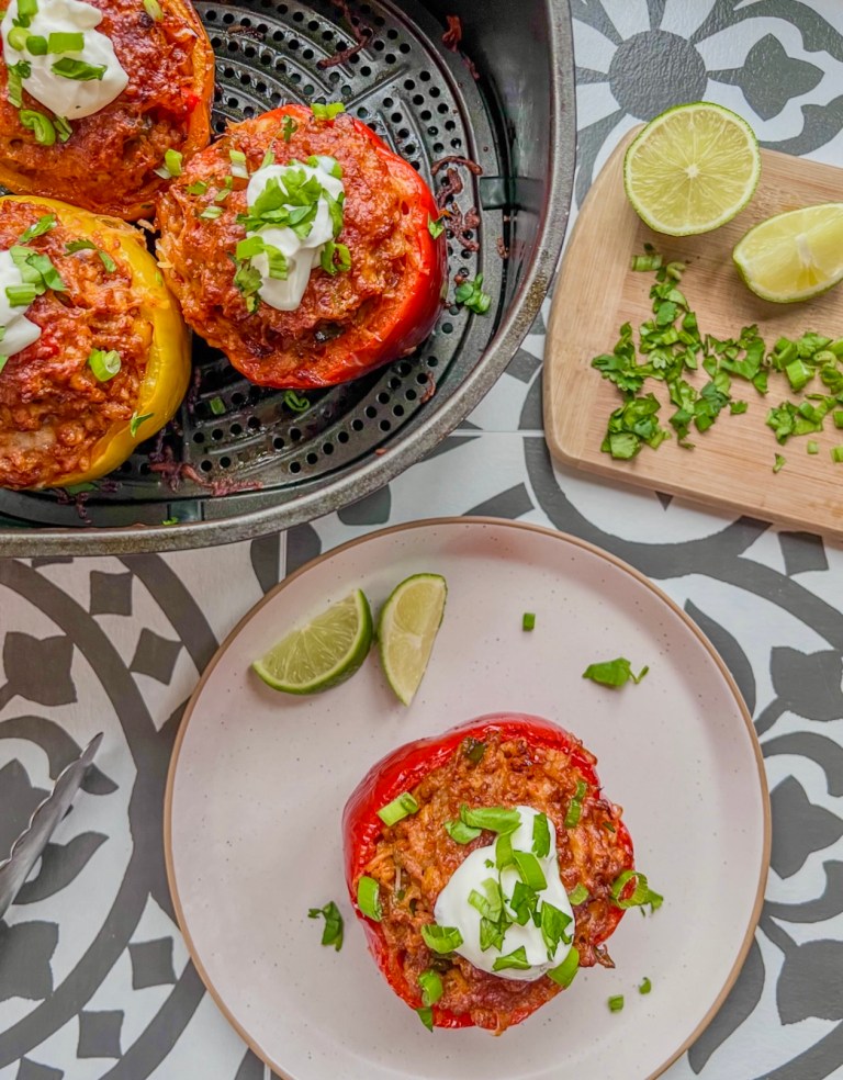 Air fryer ground chicken stuffed peppers in an air fryer basket with one on a plate and some fixings off to the side.