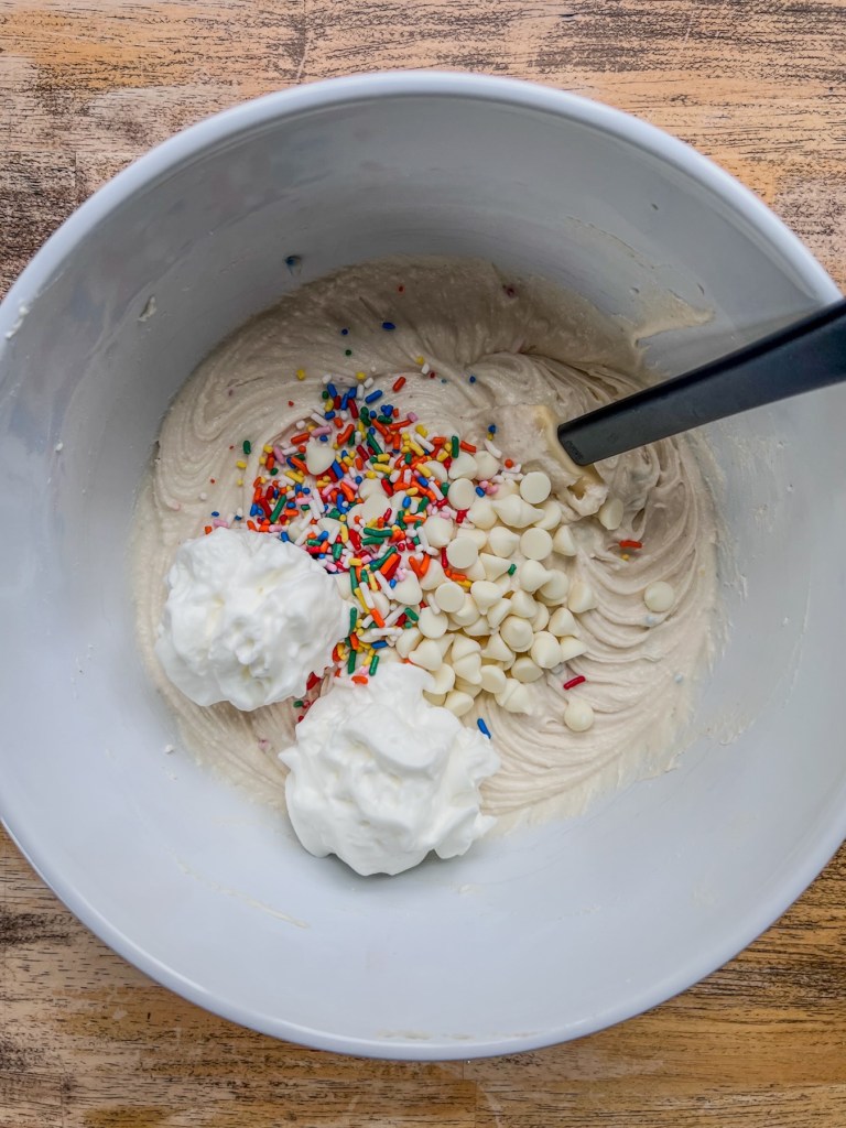 A cake batter cannoli inspired dip coming together with some freshly added whipped cream, white chocolate chips, and rainbow sprinkles