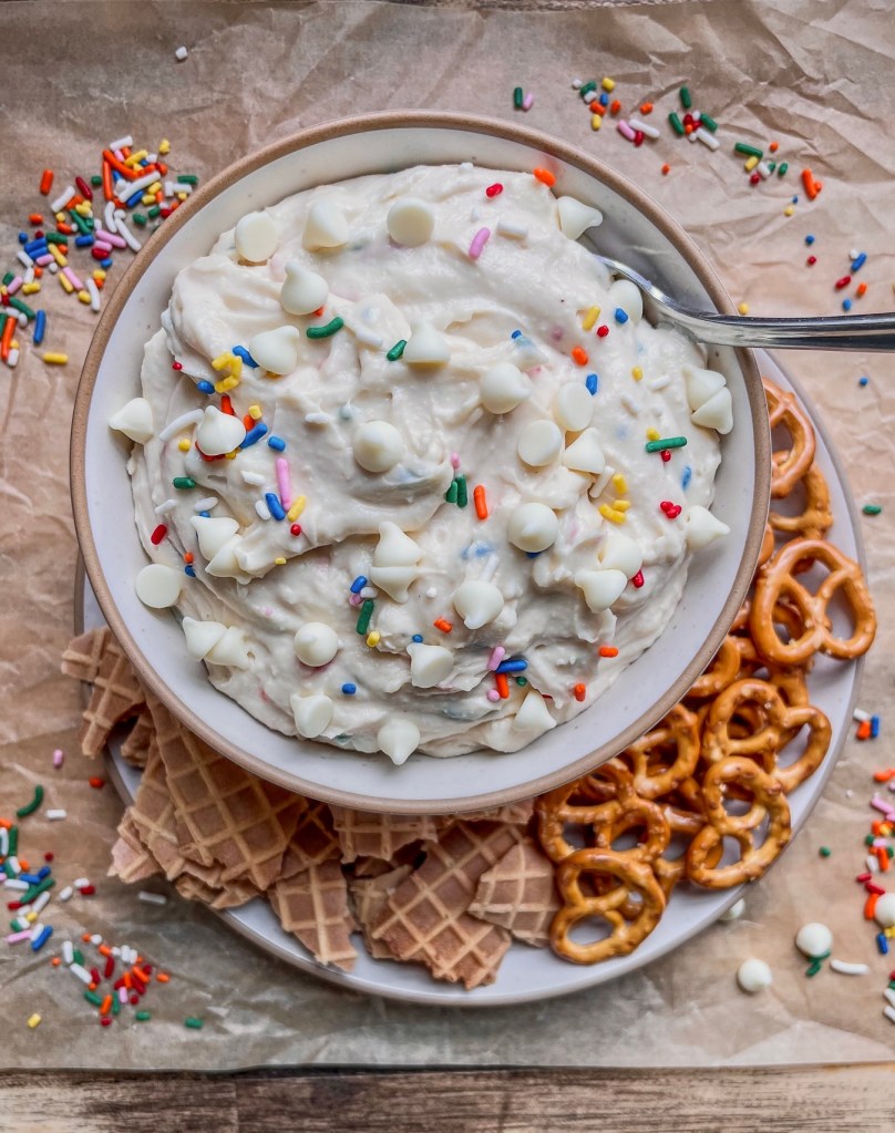 Cake Batter Cannoli dip in a bowl with some crushed waffle cones and pretzels scattered around