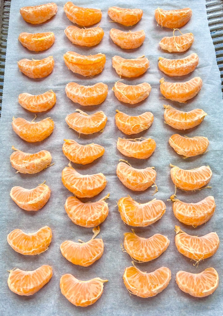 Clementine segments on a baking sheet lined with parchment paper, ready to be flash frozen