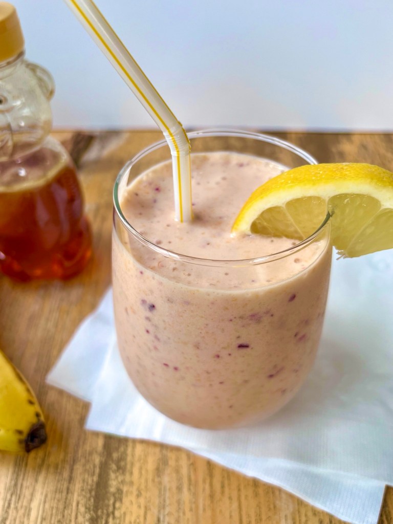 Cranberry clementine smoothie in a large glass with a lemon wedge for garnish.