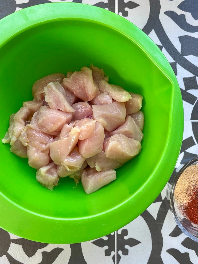 Chicken breast that's been cut into chunks and added to a bowl, just before getting tossed with oil and spices.