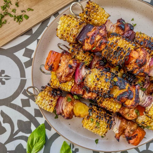 Grilled hot honey chicken skewers with rainbow carrots. Served with fresh herbs and lemon