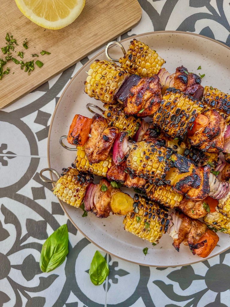 Grilled hot honey chicken skewers with rainbow carrots. Served with fresh herbs and lemon