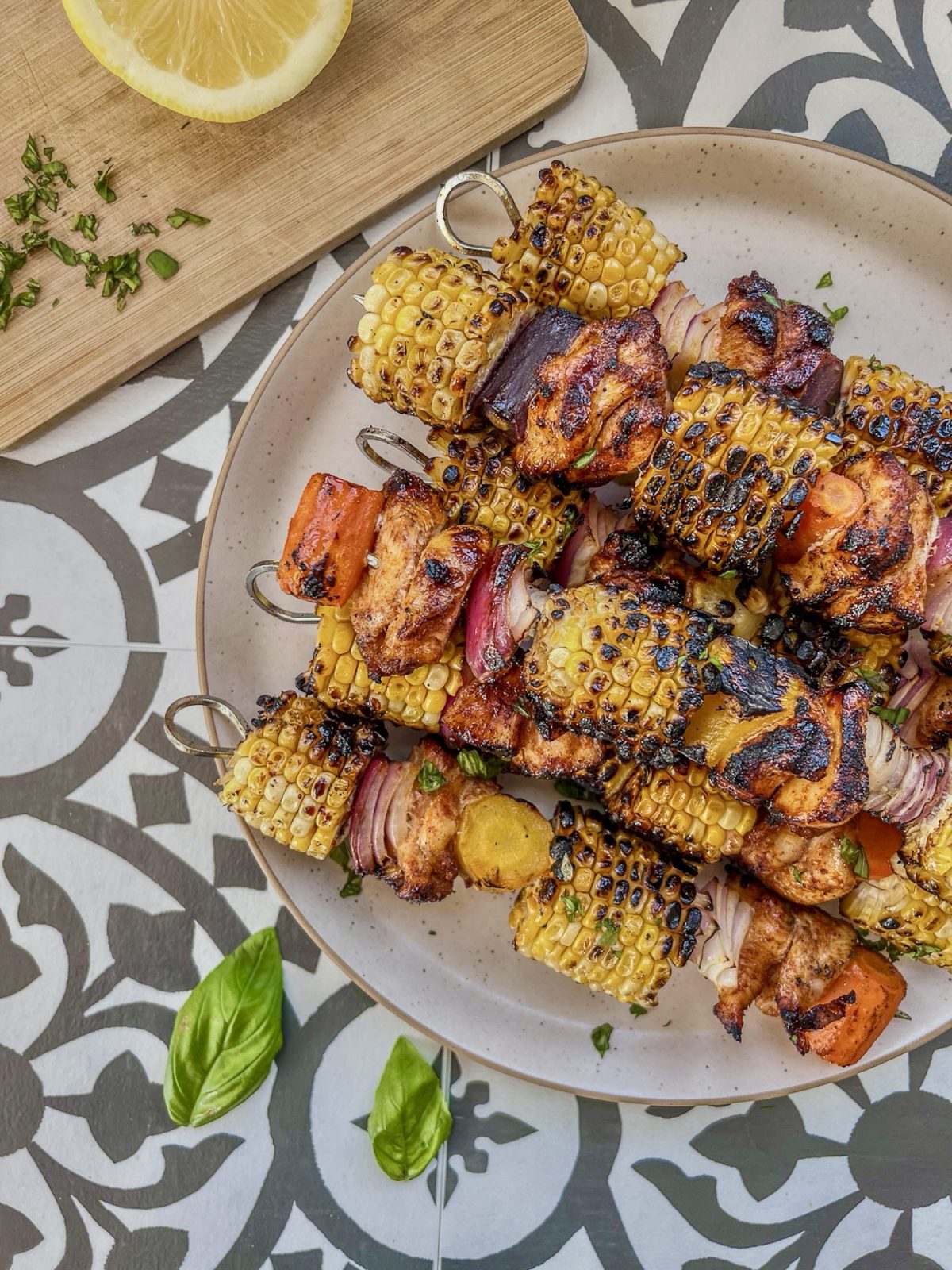 Grilled hot honey chicken skewers with rainbow carrots. Served with fresh herbs and lemon