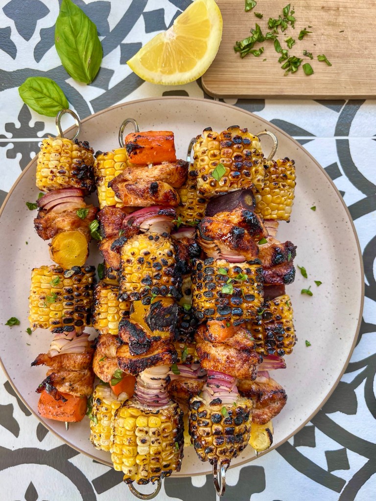 Grilled hot honey chicken skewers with rainbow carrots. Served with lemon wedges and fresh basil.