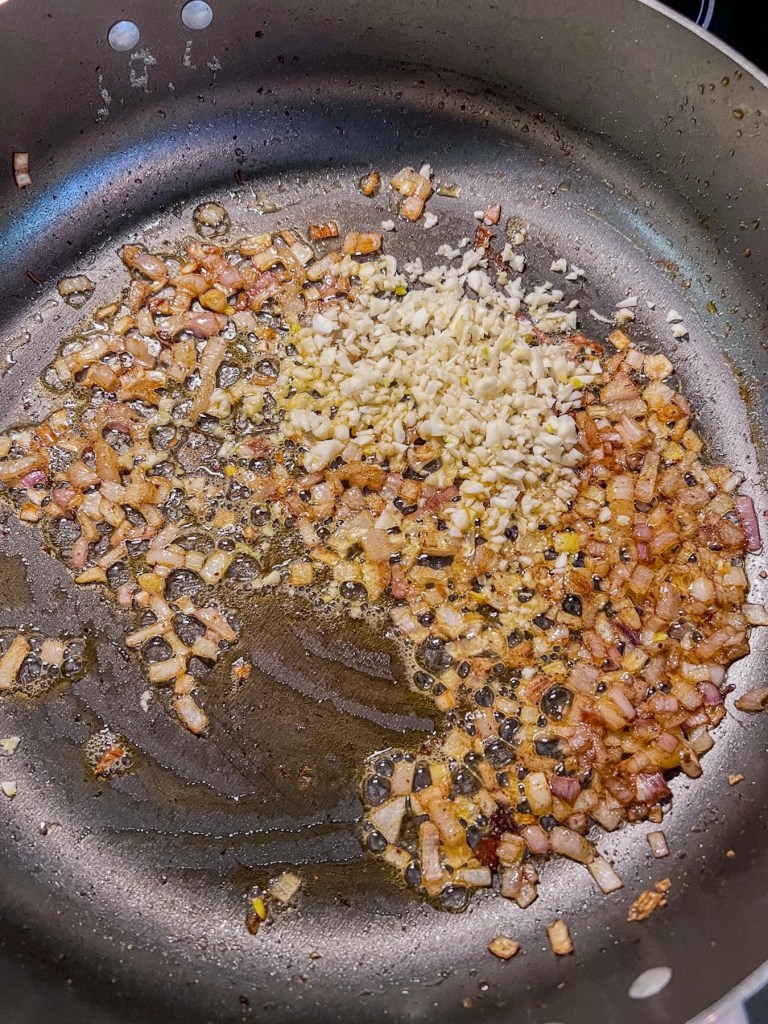 Diced shallot and minced garlic cloves sautéing in a skillet.