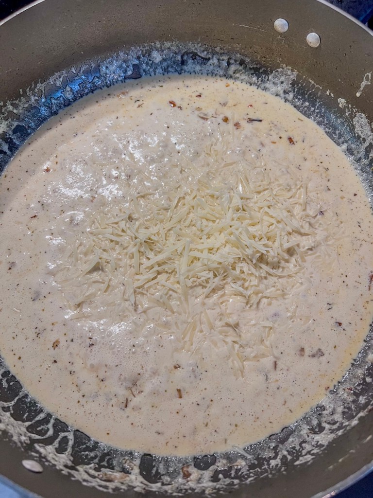 Homemade alfredo sauce cooking in a skillet on the stove