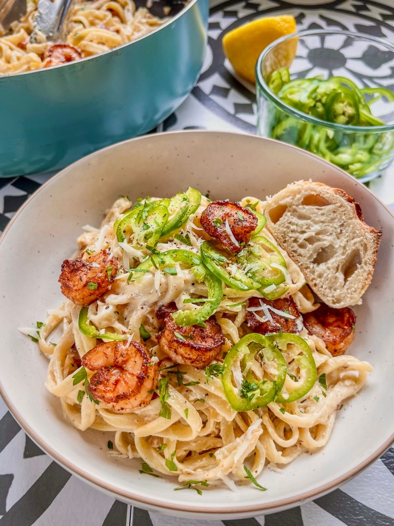 Jalapeño shrimp alfredo in a bowl with a crispy baguette and some fixings off to the side.