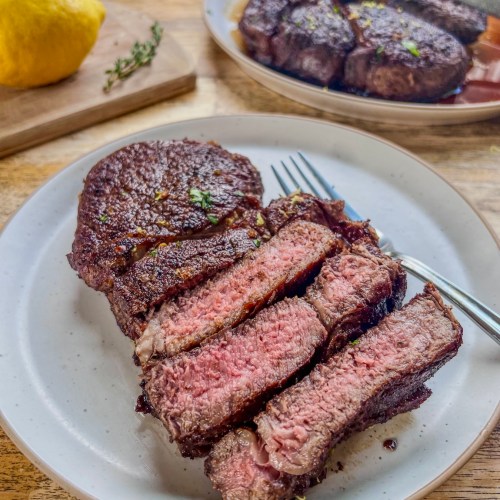 Lemon and garlic herb ribeye steaks that have been sliced and garnished with lemon zest and fresh basil