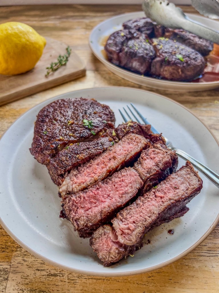 Lemon and garlic herb ribeye steaks that have been sliced and garnished with lemon zest and fresh basil