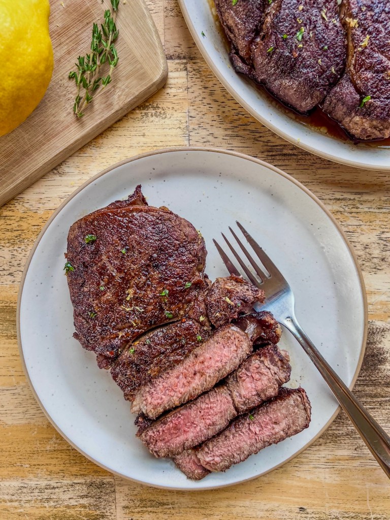 Lemon and garlic herb ribeye steaks with some fresh lemon and thyme off to the side.