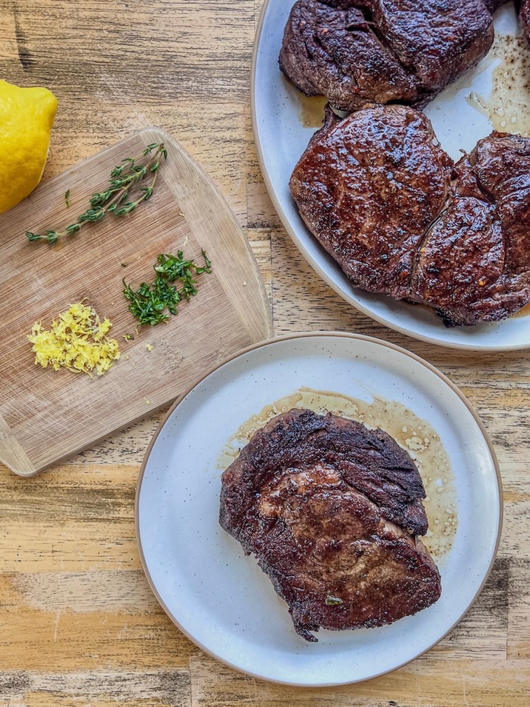 Freshly cooked steaks for dinner, served with lemon zest and fresh garden basil.