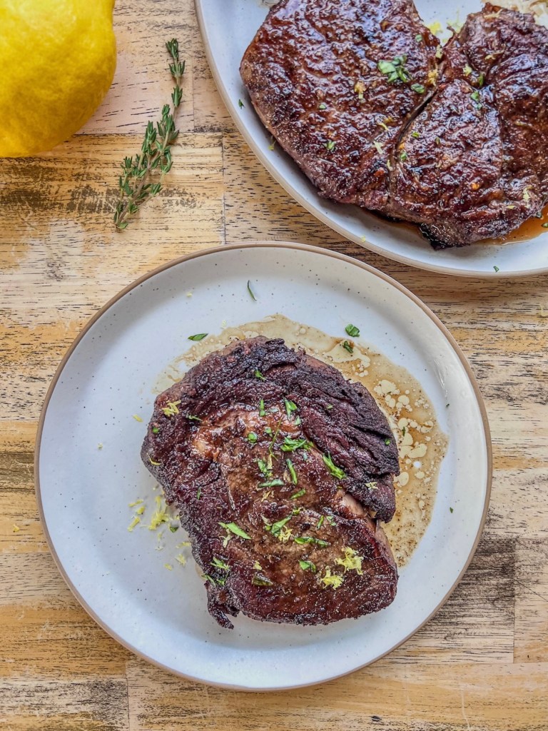 Lemon and garlic herb ribeye steaks with some lemon and fresh thyme off to the side.