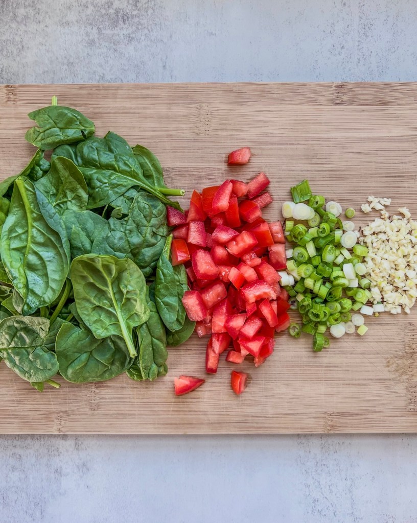 Spinach, tomato, green onion, and garlic prepped on a cutting board