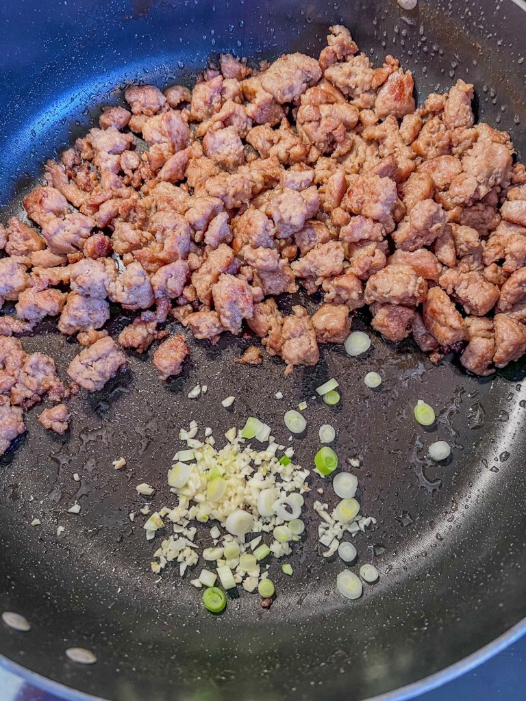 Maple breakfast sausage in a pan with some newly added green onion and garlic.