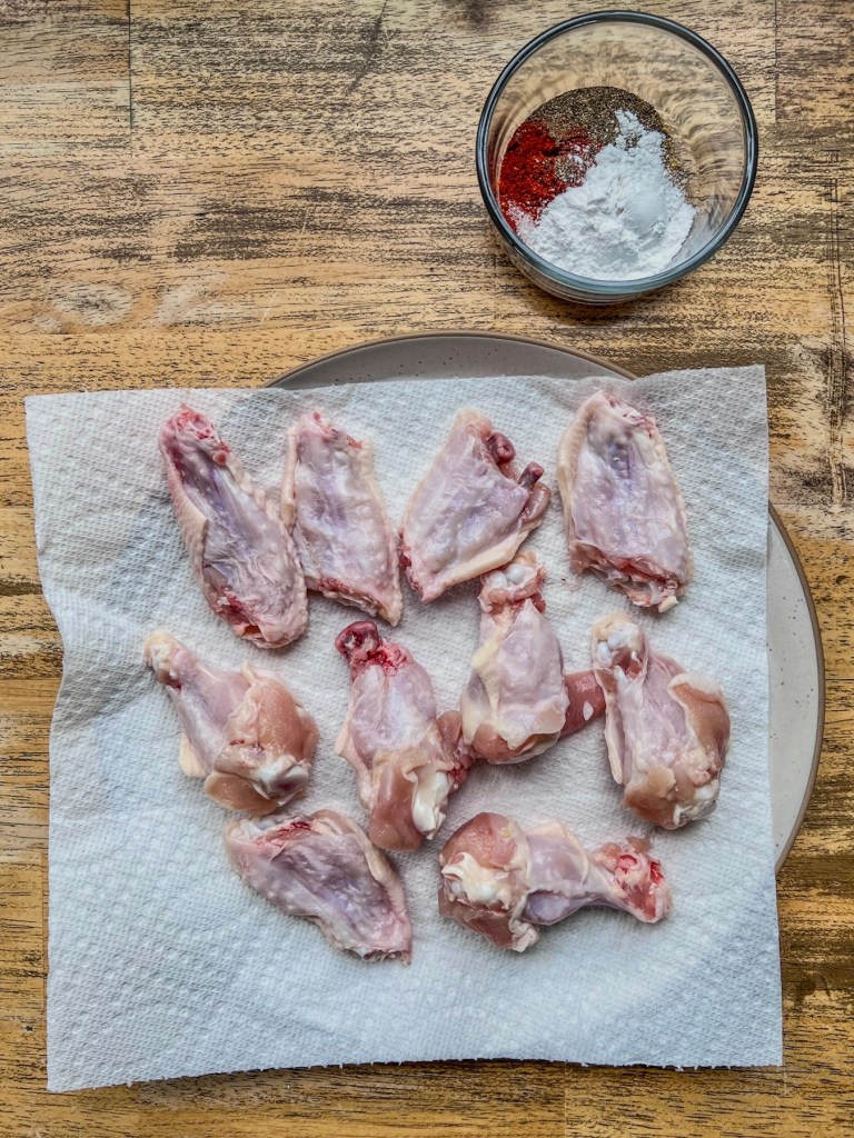 Chicken wings that have been split into drumettes and flats, with some spices off to the side.