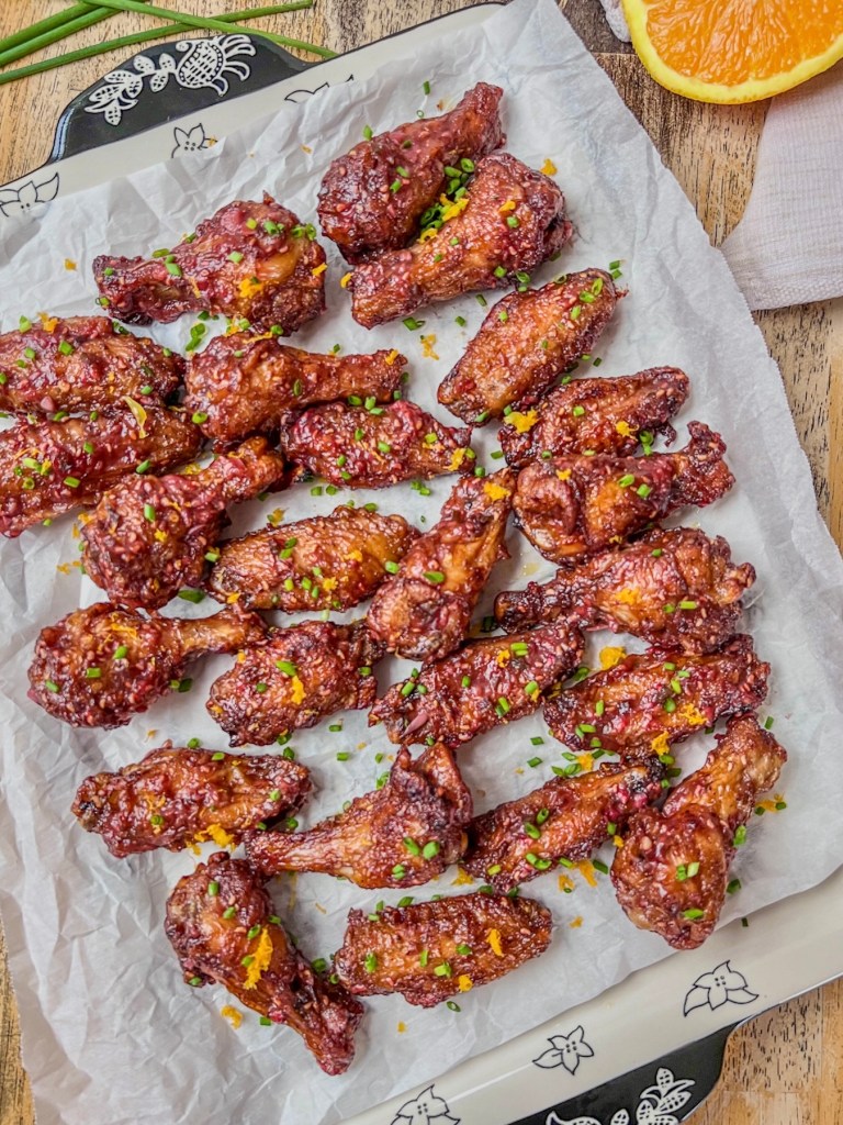 Air fryer chicken wings with a raspberry orange glaze, fresh orange zest, and chives scattered on top.
