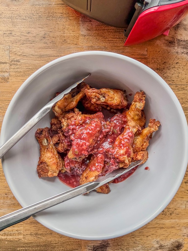 Wings getting tossed in a raspberry orange glaze in a large mixing bowl.
