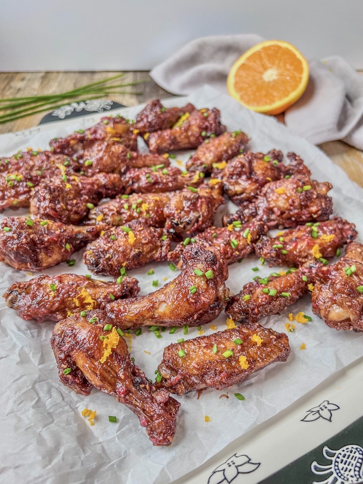 Air fryer raspberry orange chicken wings with orange zest and fresh chives scattered on top.